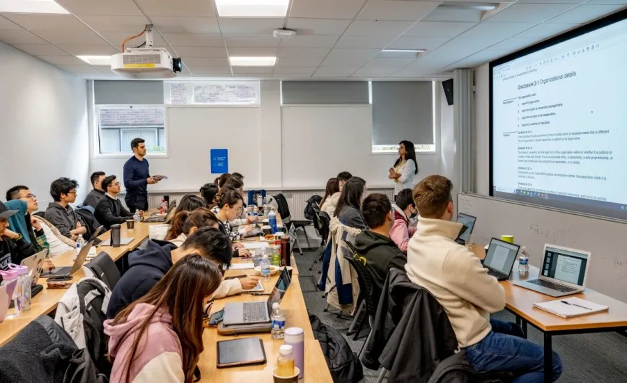 Students sitting at desks while a student is talking to the lecturer