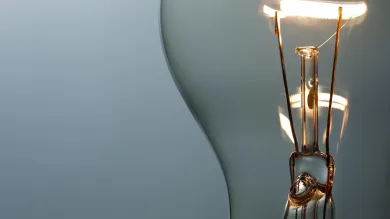 A close up of the inside of a light bulb focuses on the filament of tungsten wire that electricity runs through, a warm, lit colour in contrast to the grey background. Light bulbs are sometimes used as a way to communicate that someone's had a good idea or some insight.