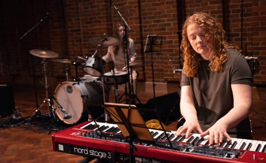 Two young musicians perform at the Turner Sims concert hall. The person in the foreground plays the keyboards, the person behind plays the drums.