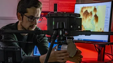 A researcher checks a remote sensing drone. To their right is a computer screen with a topographical visual