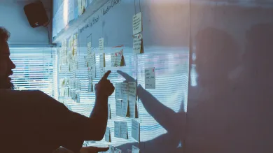 Unsplash image of post-its on a white board, a meeting participant points to a note