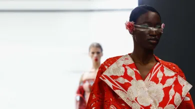 A catwalk model sports a dramatic red and white creation featuring a floral motif and outsized lapels