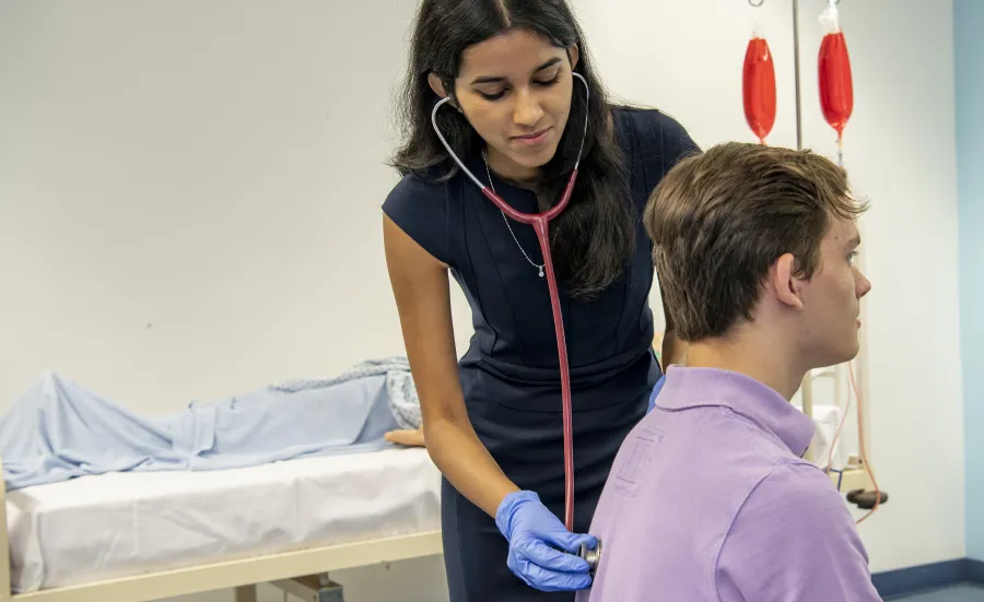 An undergraduate medicine student practices using a stethoscope on a patient in the clinical skills suite