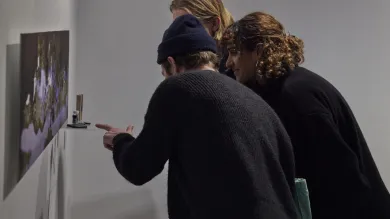 Three gallery visitors lean forward to examine an artwork hanging on the wall at The Winchester Gallery