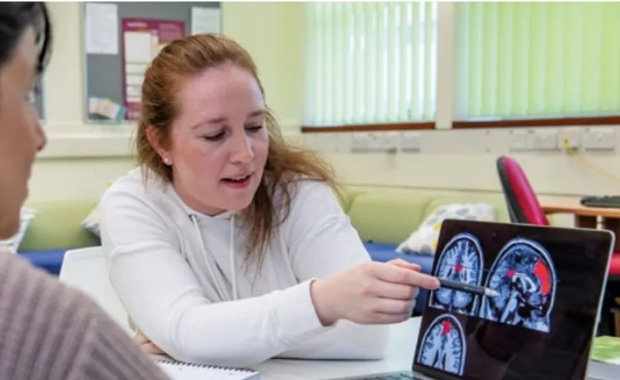 Two researchers sitting at a desk look at a tablet showing brain scan images