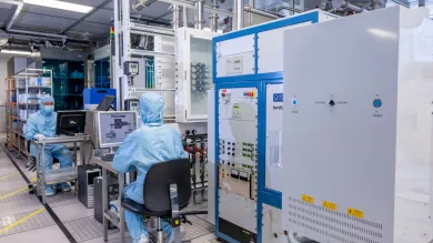 Two researchers in cleanroom suits sit at computers in the nanofabrication ballroom cleanroom