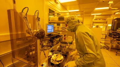 A researcher in a cleanroom suit uses the wafer bond tool