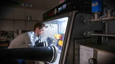 A researcher wearing safety goggles works with chemicals in a glovebox