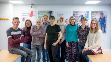 Members of the SHTAC team with Professor Joanne Lord, gathered around a bright room with various posters in the background. 