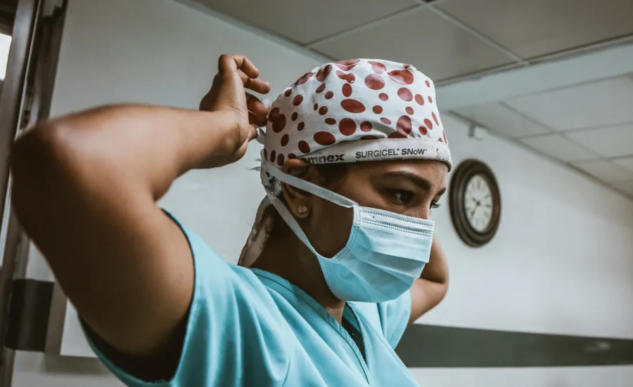 a medical practitioner adjusts their surgical cap, looking intently ahead..
