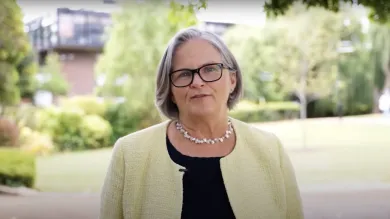 Deborah Gill talking directly to the camera with university grounds in the background.