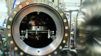 large, cylindrical metal chamber, likely part of scientific or industrial equipment. The chamber is open, revealing a complex mechanism inside. 