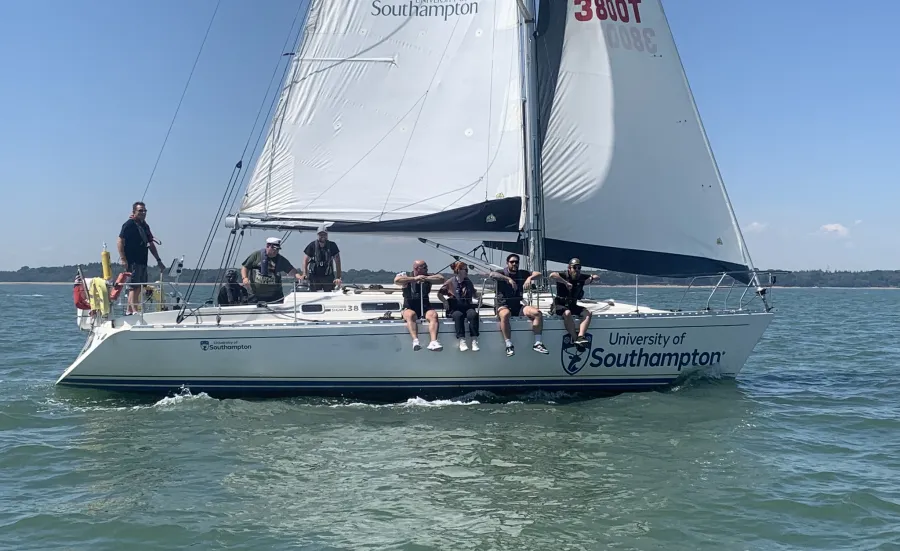 Crew sitting on the side of a yacht sailing on the sea.