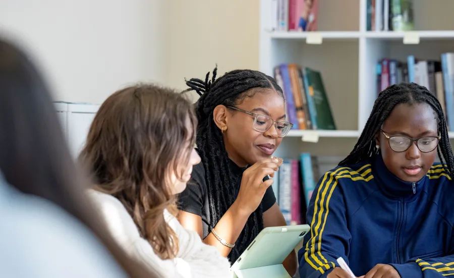 Psychology students sitting around a table. They are writing and mapping out work on a large piece of paper on the table. There are book shelves in the background.