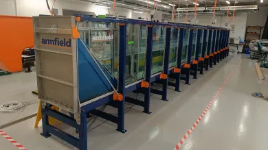 Long glass-sided wave tank in a laboratory, supported by a blue metal frame with orange fittings, and an Armfield wave generator positioned at one end.
