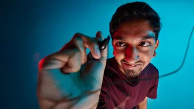 A student using a black marker pen to draw a line on a glass screen. The student is wearing a dark red t-shirt and is positioned in front of a blue background.