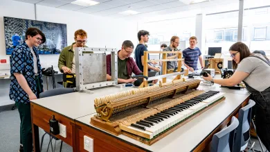 A group of students sits around a long table in a classroom, where a piano keyboard has been placed for an experiment.
