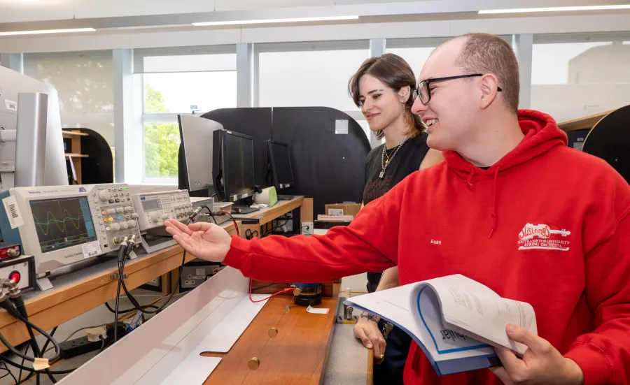 Two students in a physics laboratory using a variety of equipment, including a digital oscilloscope and a DDS function generator.