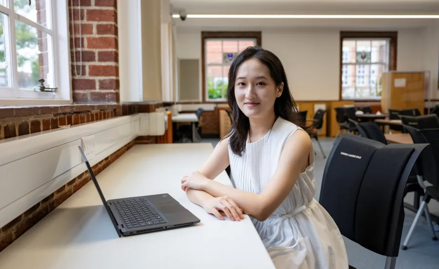 Lin sitting at a desk in an empty classroom. She has a laptop on the desk in front of her, and she's smiling for the camera.