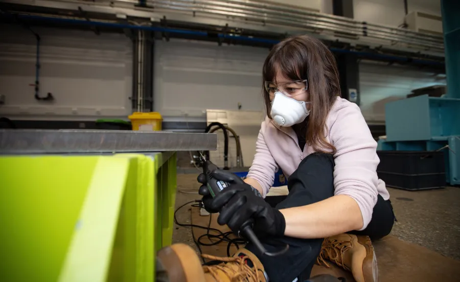 A researcher wearing protective equipment uses a handheld power tool inside the National Infrastructure Laboratory.