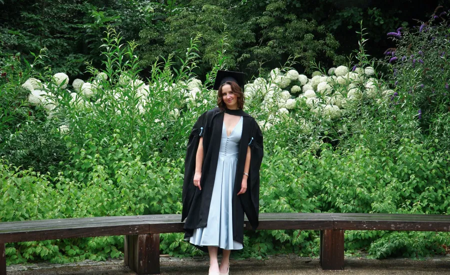 Isabelle, a BSc Pharmacology student, posing for a graduation photo in front of vibrant green foliage and white flowers. 