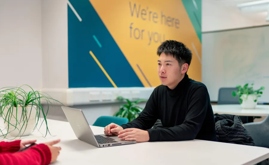 Student using a laptop during a one-to-one careers support conversation in a campus space.