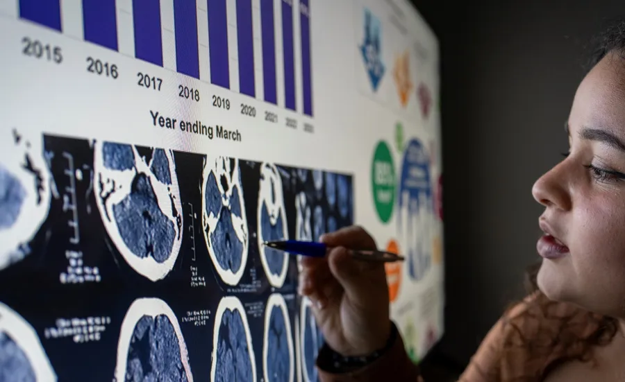 A person closely examining a large digital display of brain scan imagery.