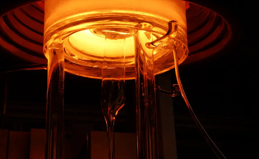 Glowing furnace with glass rods extending downward, emitting orange light.