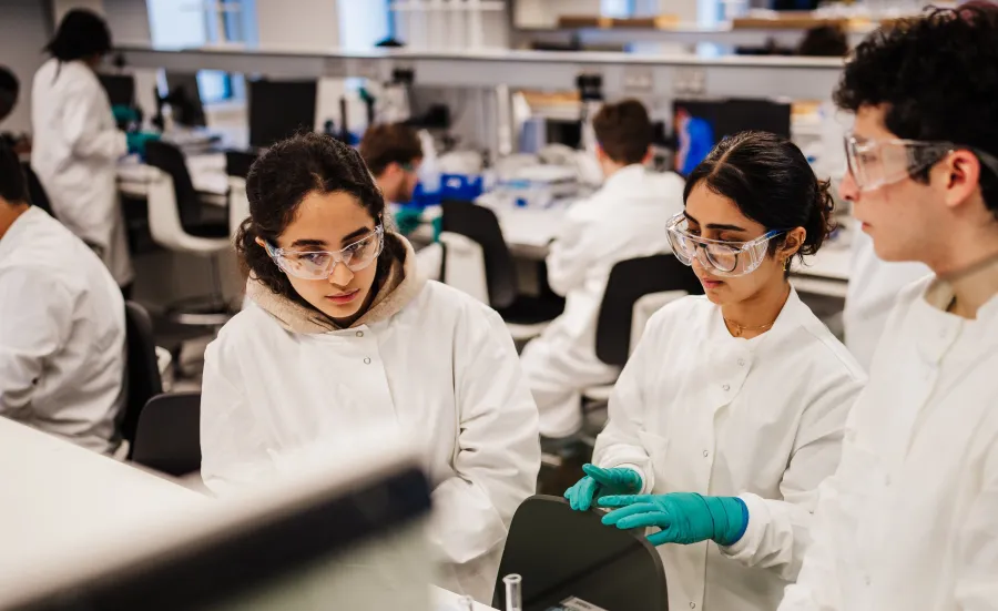 University students in lab coats and safety goggles working together in a modern science laboratory.