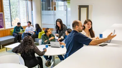 Students collaborate in small groups supervised by a tutor in a bright, modern learning space.