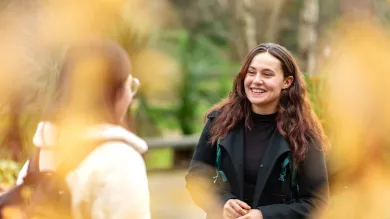 An undergraduate student stood outside talking to someone and smiling.