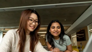 Two international students research courses on a laptop