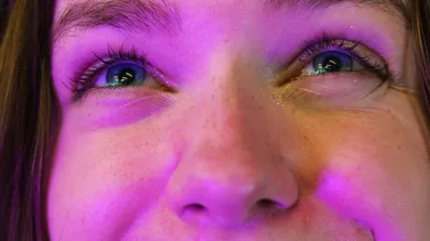The camera leans close to the face of a student bathed in a warm purple light. She looks up, smiling expectantly