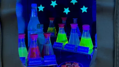 Bottles and laboratory flasks containing fluorescent liquids glowing under ultraviolet light.
