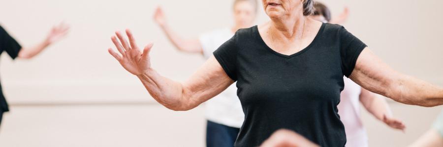 An older woman with grey hair and a black top takes part in a fitness class