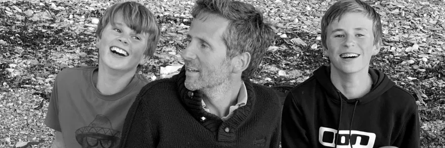 A monochrome photo of Crispin Malpas and his sons in a casual moment, enjoying each others' company.