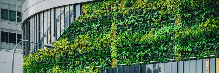 A modern building in an urban environment covered with glass panels and greenery.