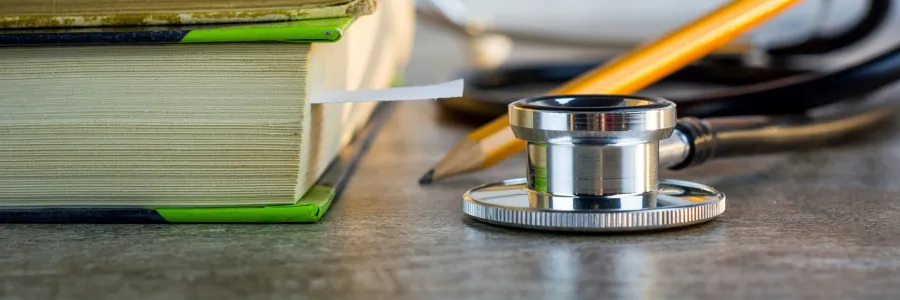 Stack of books with a stethoscope and pencil in front.