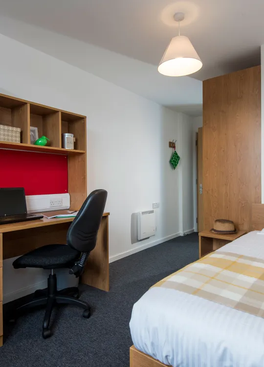 A modern student bedroom with white walls, wooden desk and neatly made double bed.