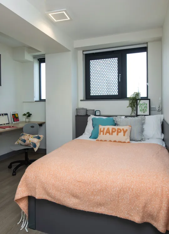 An standard en-suite room at Capital House. A desk is sat in an alcove at the back left corner of the room, and there's a bed against the wall to the right side of the room.