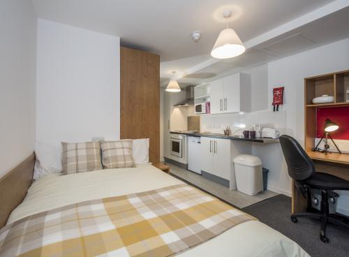 A modern studio flat showing bed, desk and kitchenette.