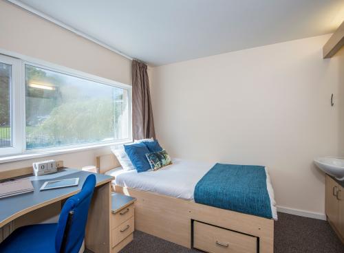 A large window lets light into a bedroom where a neatly made double bed, wash basin and desk can be seen.
