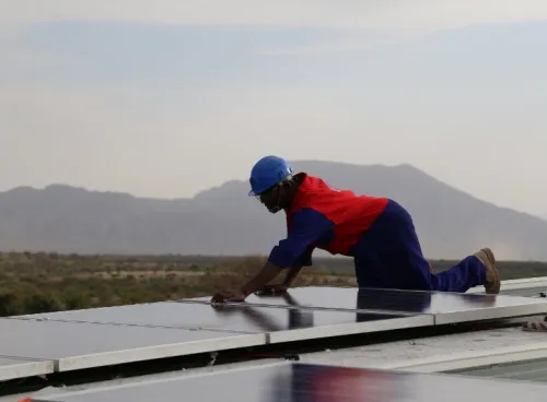 person wearing construction clothing fitting solar panels for renewable energy on roof in kenya