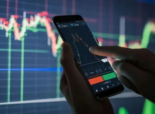 Image of a data graph and a mobile phone in someone's hands, which displays financial information.