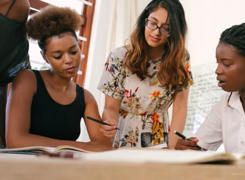 Diverse group of women collaborating round a table, using pens and paper