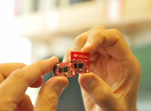 Hand holding a red internet of things circuit board created by the Centre for IoT and Pervasive Systems. 
