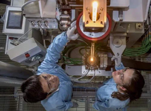 View from above of two researchers feeding glass into a fibre drawing furnace.