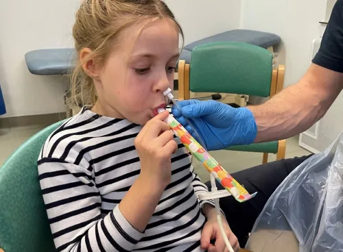 Young girl with a tube up her left nostril, blowing a party blower