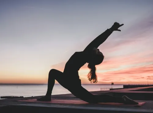 Silhouette of a person doing yoga by the water at sunset.