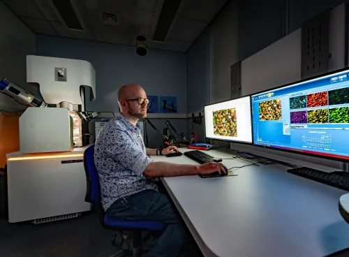 A technician works at computers displaying microscopic images, with a TESCAN electron microscope nearby.